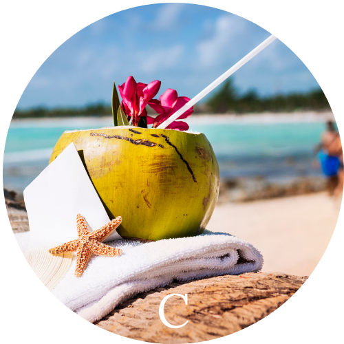 Coconut filled with a rum cocktail sitting on a towel with a starfish on a beach