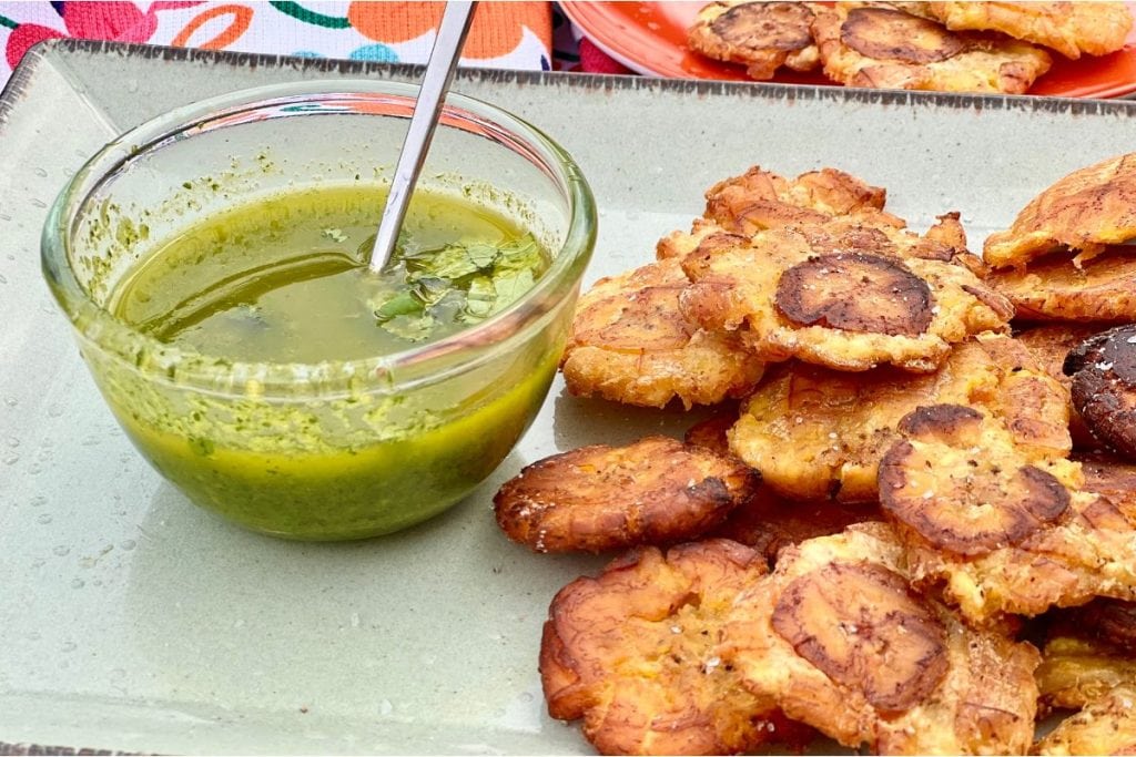 Tostones or Fried Green plantains sitting of a plate with a bowl of cilantro garlic dipping sauce
