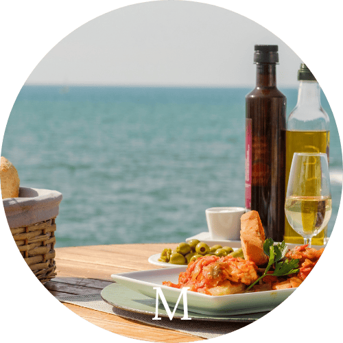 bruschetta, olives, bread on a table with olive oil, vinegar and wine overlooking the water representing Mediterranean Cuisine