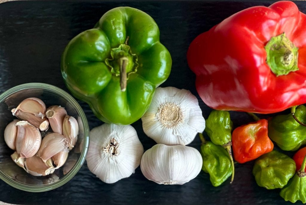 overhead shot of red and green peppers, garlic and aji dulce peppers on a black tray