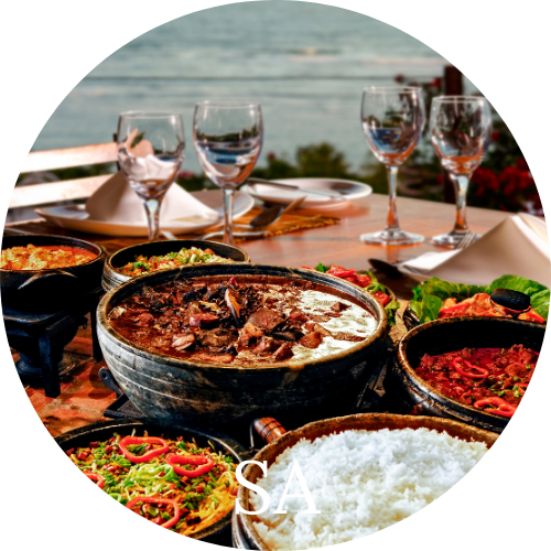Bowls of Stews and Rice on a wood table with wine glasses overlooking the water representing South American cuisine