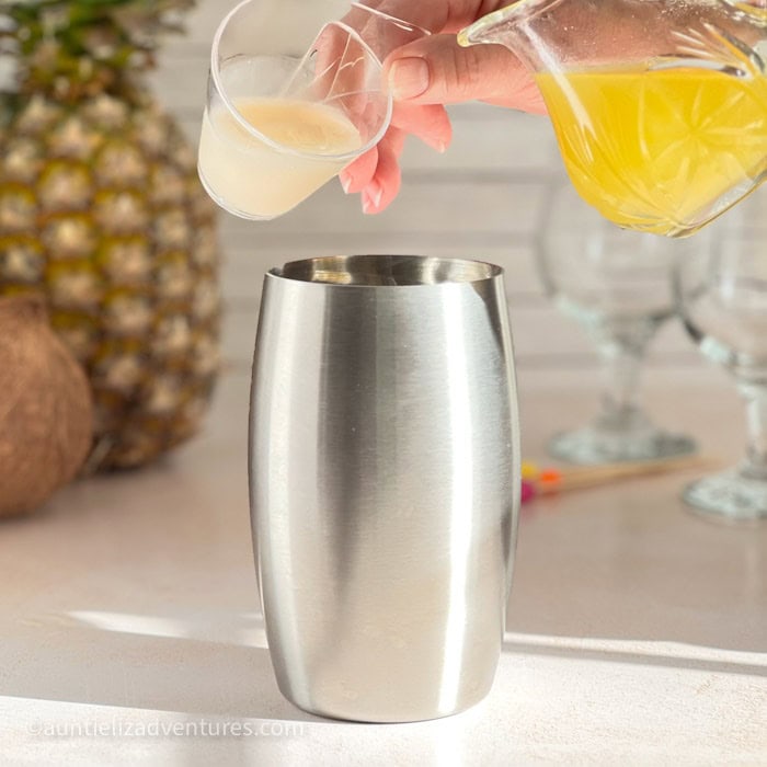 Step 2 of making a Pina Colada, pouring cream coconut and pineapple juice into cocktail shaker