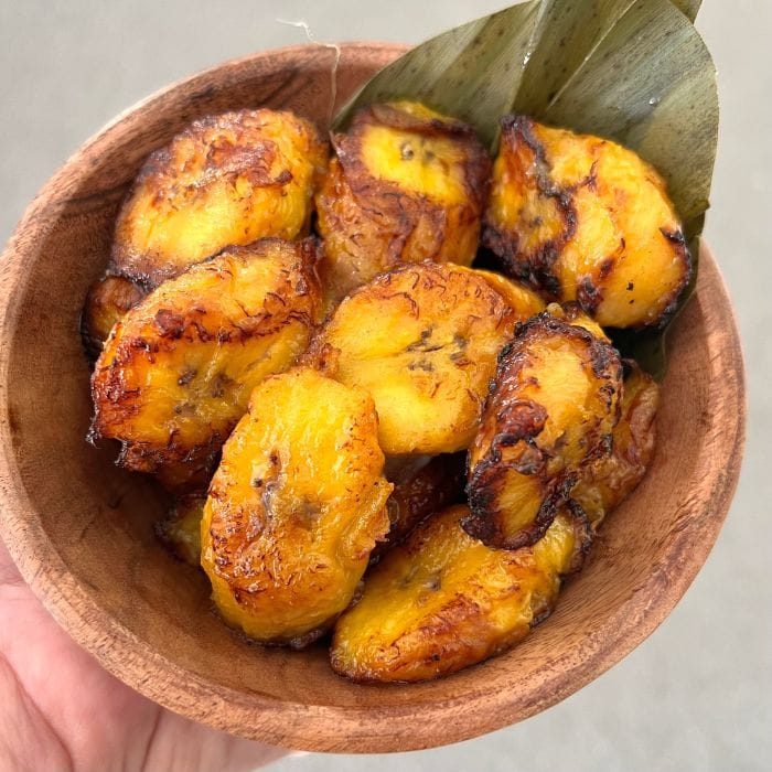 Golden fried sweet plantains in a wood bowl with a plantain leaf garnish.
