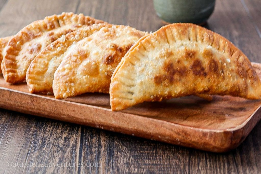 5 beef empanadas sitting on a rectangular wood plate on a wood table