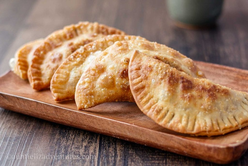 5 beef empanadas sitting on a rectangular wood plate on a wood table