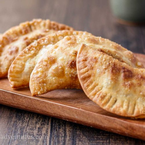 5 beef empanadas sitting on a rectangular wood plate on a wood table