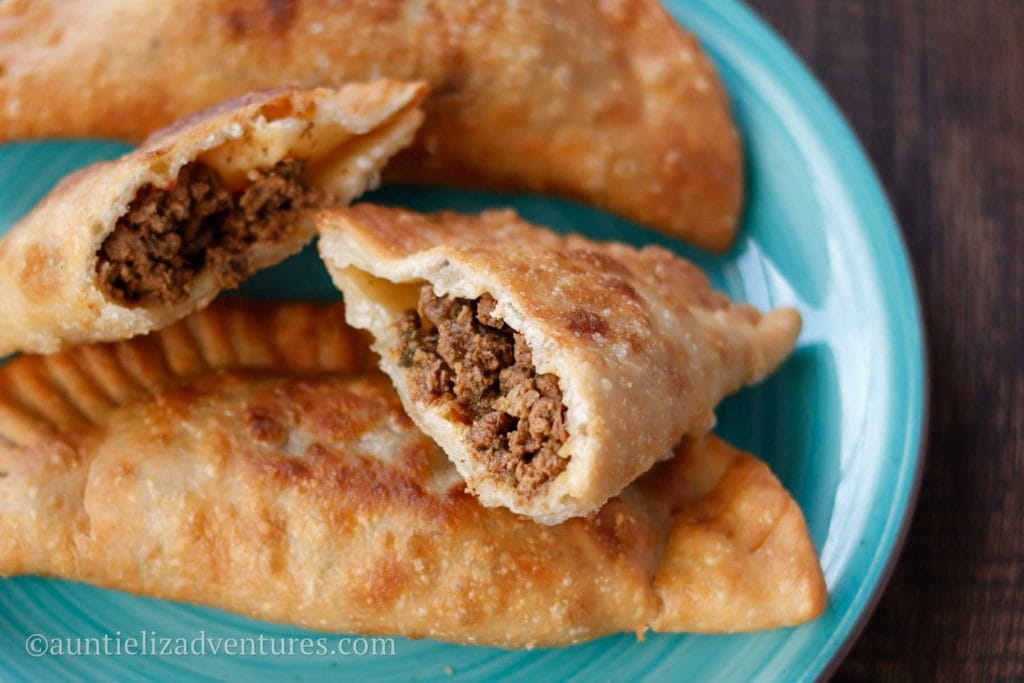 3 beef empanadas on a aqua blue plate with one cut open showing ground beef filling